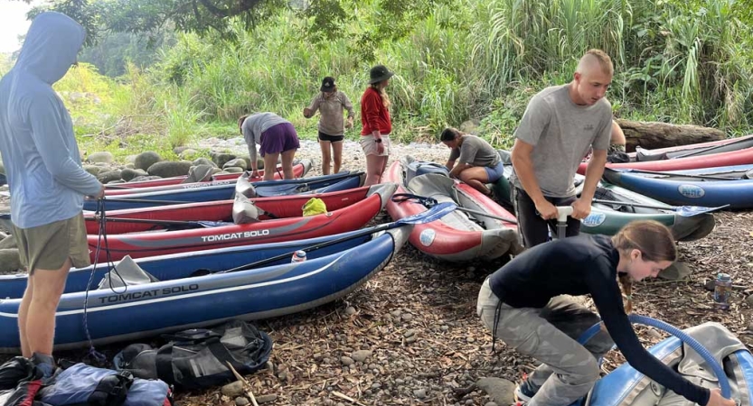 A group of students move around beached watercraft on a shore. 